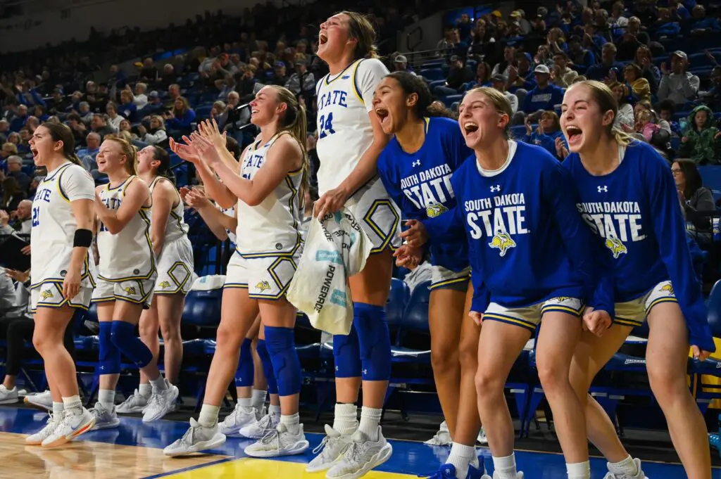 The South Dakota State basketball bench cheers during a 2025 NCAA game.