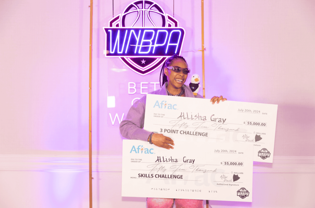 Atlanta Dream guard Allisha Gray smiles while holding her 2024 WNBA All-Star 3-Point Contest and Skills Challenge champion checks.