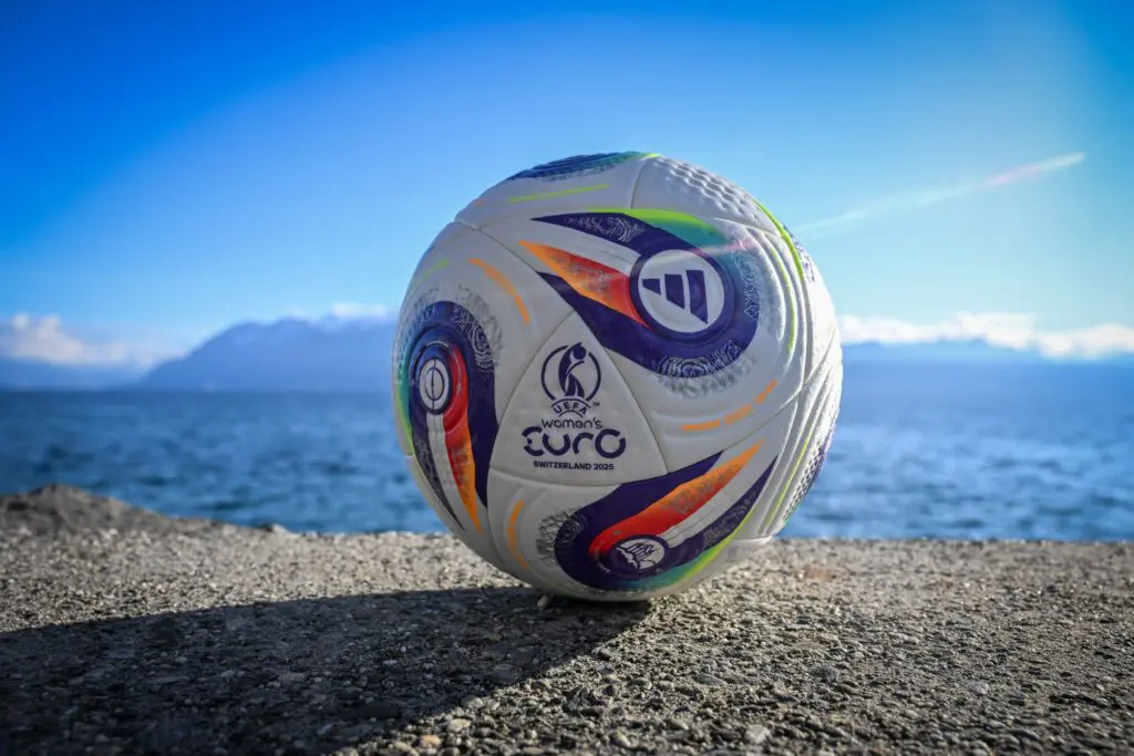 An official 2025 UEFA Women's Euro soccer ball rests on the ground in front of a lake in Switzerland.