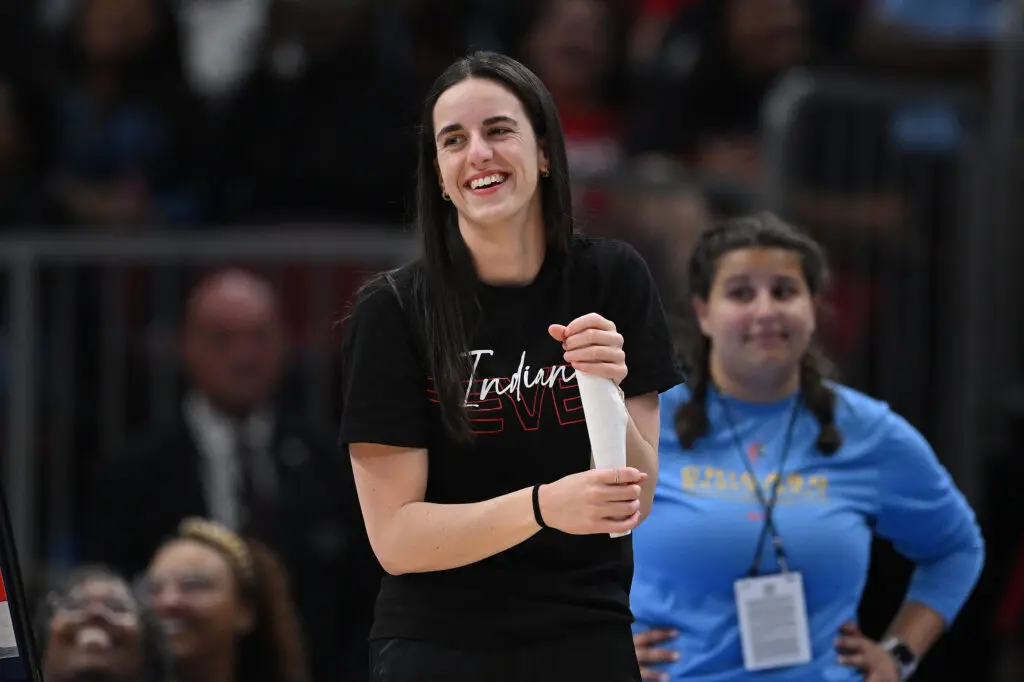 Injured Indiana Fever guard Caitlin Clark smiles from the sideline during a 2025 WNBA game.