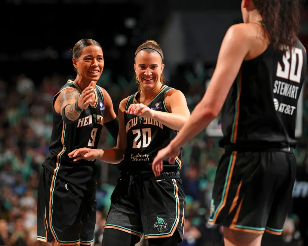 New York Liberty stars Natasha Cloud and Sabrina Ionescu celebrate with teammate Breanna Stewart during a 2025 WNBA game.