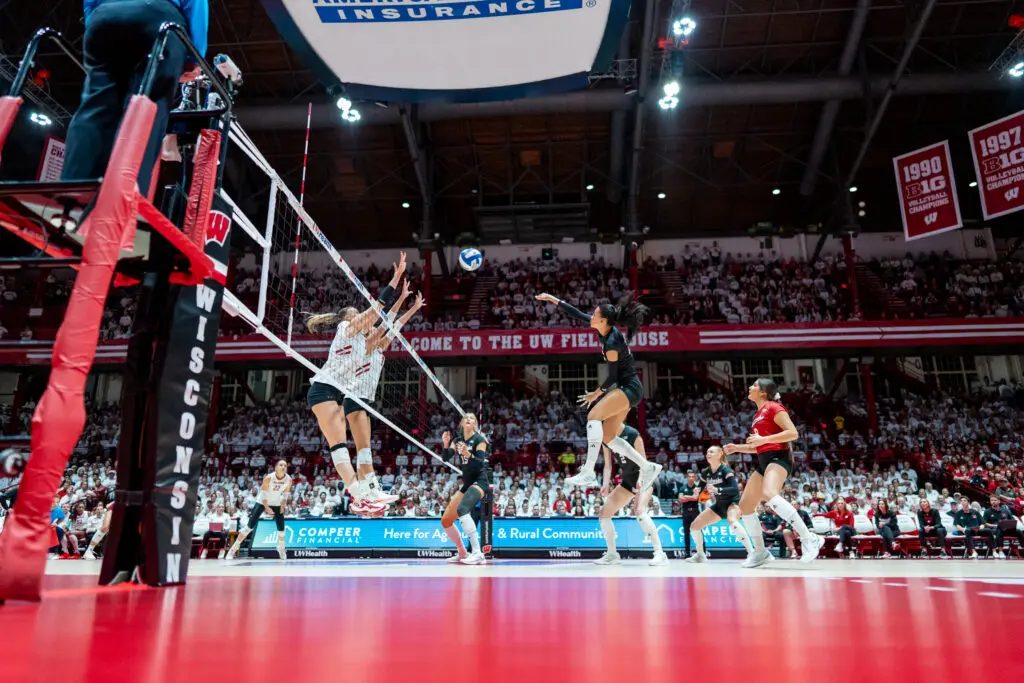 Wisconsin volleyball players leap to block a kill from rival Nebraska during a 2024 NCAA match.