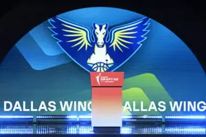 The Dallas Wings name and logo covers the stage at the 2025 WNBA Draft during one of the team's selection announcements.