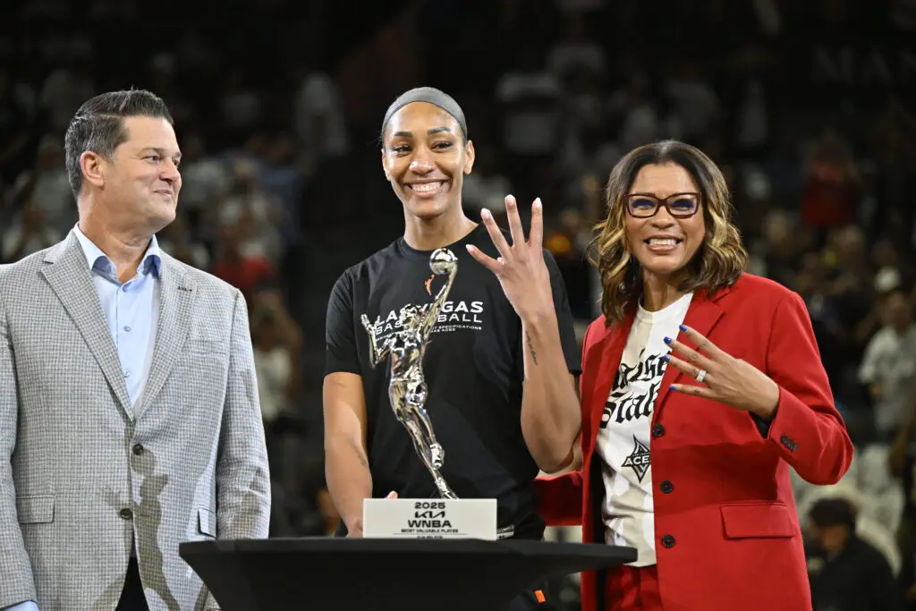 Las Vegas star A'ja Wilson holds up four fingers as she poses with her 2025 WNBA MVP trophy alongside Aces president Nikki Fargas and head of league operations Eric Watson before the semifinals' Game 1.