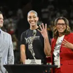 Las Vegas star A'ja Wilson holds up four fingers as she poses with her 2025 WNBA MVP trophy alongside Aces president Nikki Fargas and head of league operations Eric Watson before the semifinals' Game 1.