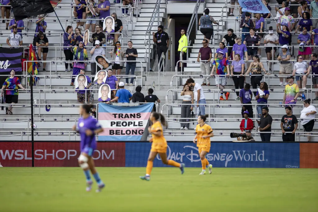 NWSL fans display a flag reading "Trans People Belong" at a 2025 NWSL match during Pride Month.