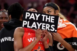 WNBA All-Stars Brittney Sykes and Angel Reese hold a sign reading "Pay the Players" after the 2025 All-Star Game.
