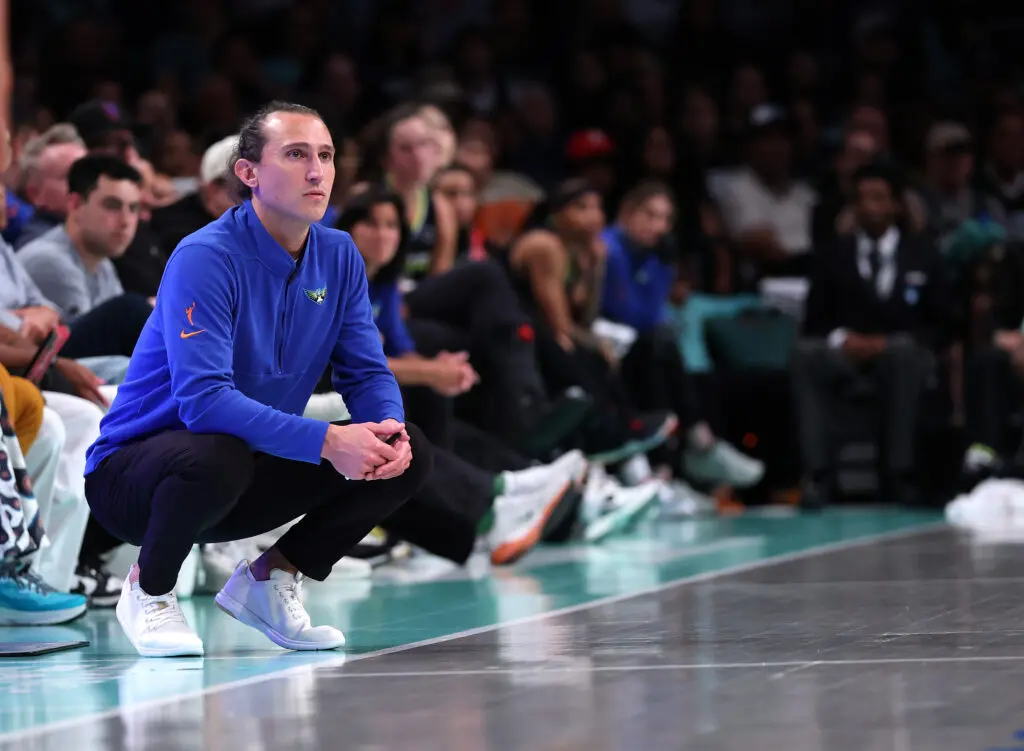 Dallas Wings head coach Chris Koclanes crouches on the sideline watching a 2025 WNBA game.