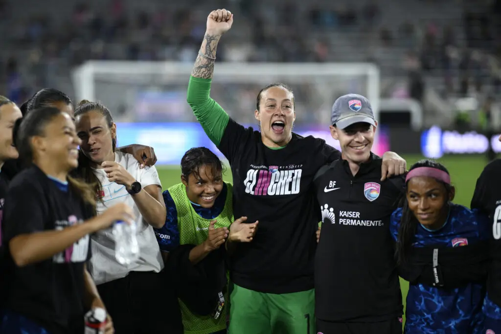 Goalkeeper Kailen Sheridan raises her arm in triumph in a San Diego Wave huddle after a 2025 NWSL match.
