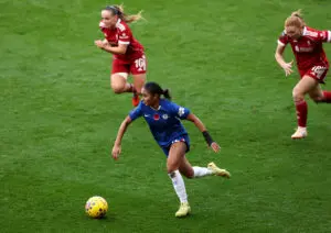 A pair of Liverpool defenders chase Chelsea FC forward Alyssa Thompson as she takes the ball up the pitch during a 2025/26 WSL match.