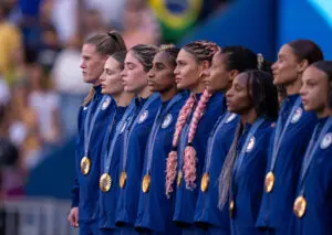 The USWNT stand on the podium wearing their gold medals at the 2024 Paris Olympics.