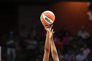 Two players' arms reach for the basketball during tipoff at a 2025 WNBA game.