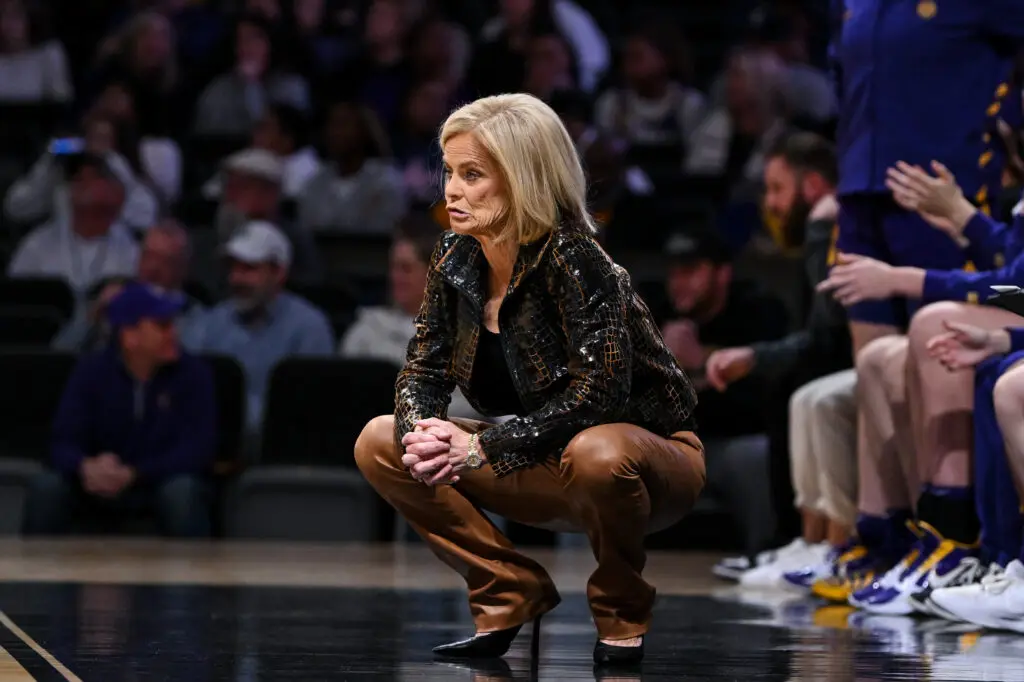 LSU head coach Kim Mulkey frowns as she squats down on the sideline during a 2025/26 NCAA basketball game.