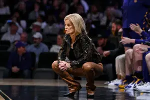 LSU head coach Kim Mulkey frowns as she squats down on the sideline during a 2025/26 NCAA basketball game.
