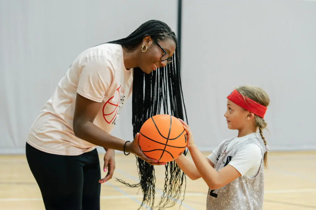WNBA star Aliyah Boston hands a basketball to a girl at a YMCA training camp.