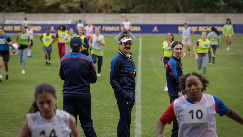 A season 4 still from Apple TV's "Ted Lasso" shows actors Brendan Hunt, Jason Sudeikis, and Tanya Reynolds in a scene of a women's soccer practice.