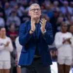 UConn head coach Geno Auriemma applauds a tribute video for past teams before a 2025/26 NCAA basketball game.