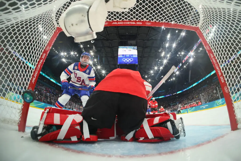 USA hockey forward Alex Carpenter flips the puck into the goal past Switzerland goaltender Andrea Brändli during a group-play game at the 2026 Winter Olympics.