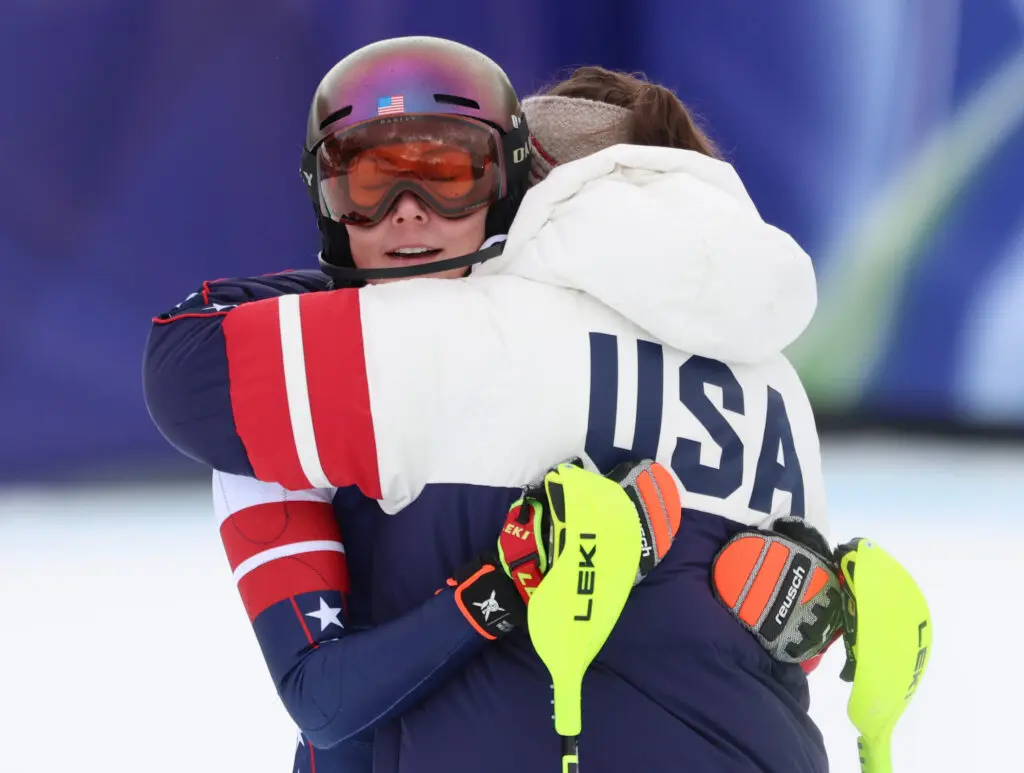 USA ski star Mikaela Shiffrin hugs a teammate after a disappointing slalom run in the women's team combined at the 2026 Winter Olympics.