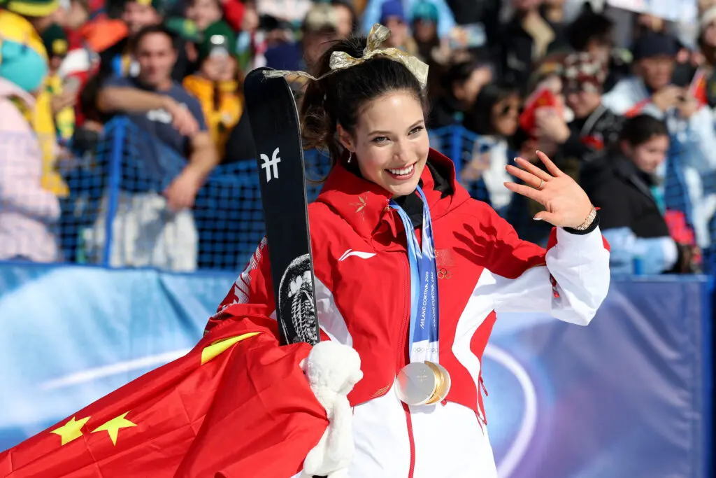Chinese freeskiier Eileen Gu waves to the crowd during the medal ceremony after winning halfpipe gold on the last day of the 2026 Winter Olympics.