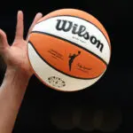 A hand reaches up to tip off a WNBA basketball during a 2024 game.