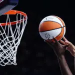 Two players' hands reach for the ball near the basket during a 2025 WNBA game.