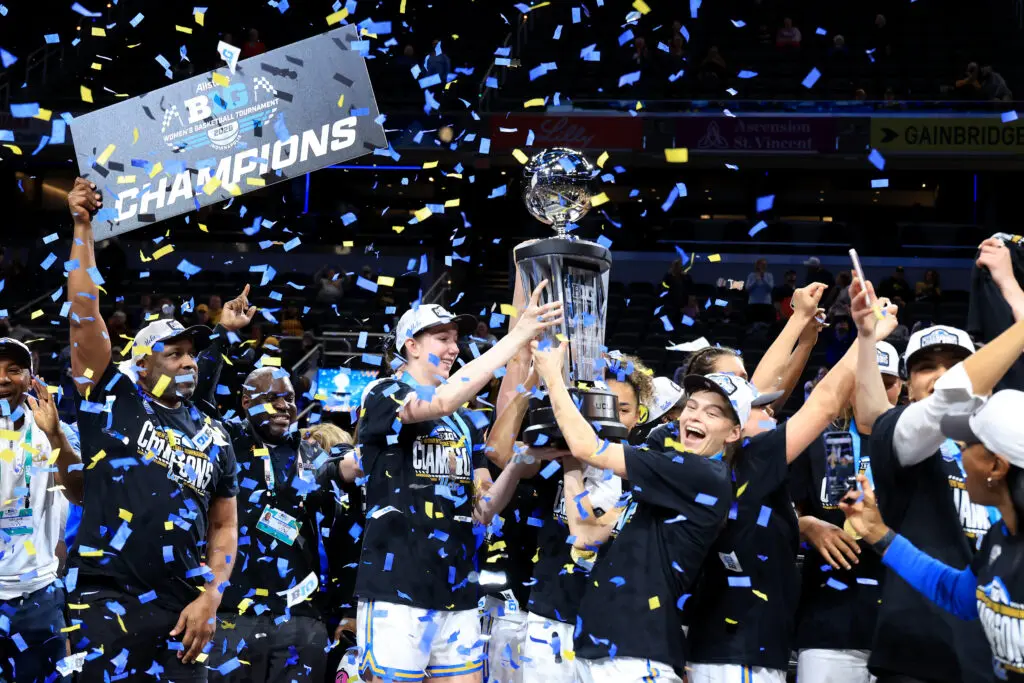 UCLA players lift the 2026 Big Ten basketball tournament trophy in celebration while confetti falls.