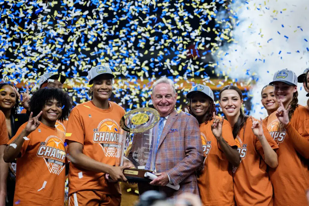 Surrounded by the team, Texas forward Madison Booker and head coach Vic Schaefer hold the 2026 SEC basketball tournament trophy as confetti rains down.