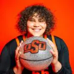 Oklahoma State NCAA transfer portal pickup Audi Crooks poses with a silver and orange OSU basketball against an orange backdrop.