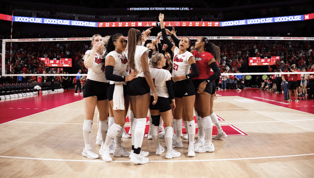 Nebraska Cornhuskers women's volleyball team celebrates at the net.
