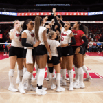 Nebraska Cornhuskers women's volleyball team celebrates at the net.