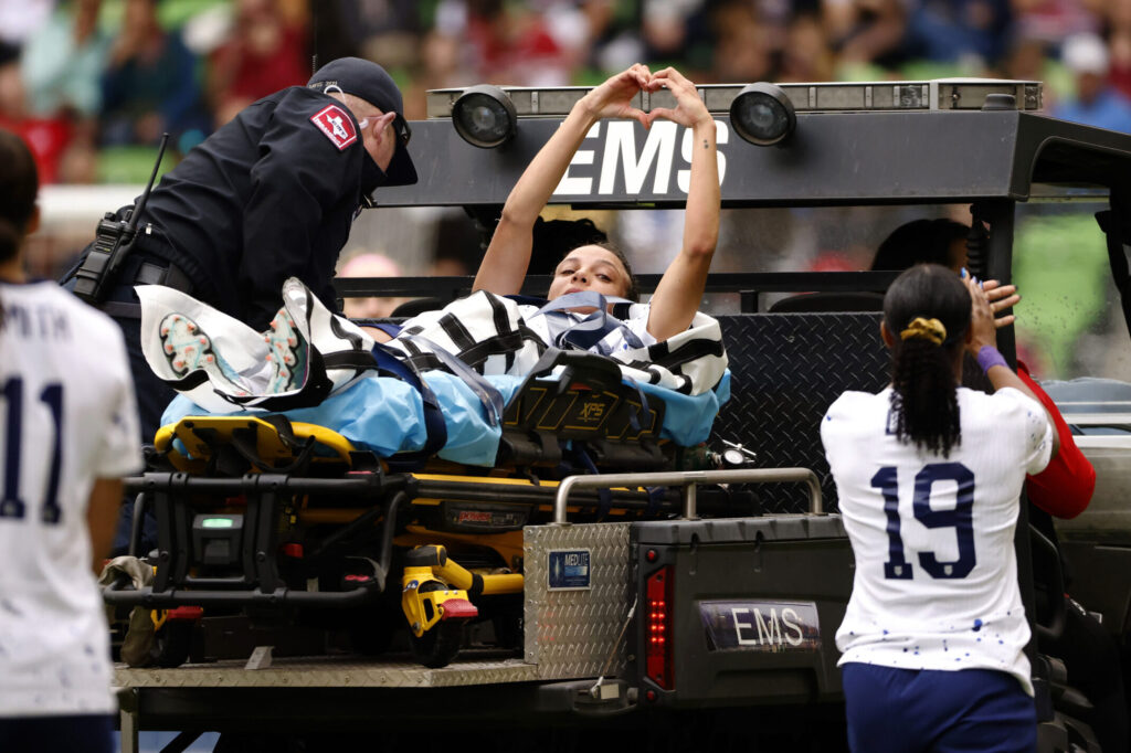 Mallory Swanson makes a heart with her hands as she is stretchered off the field