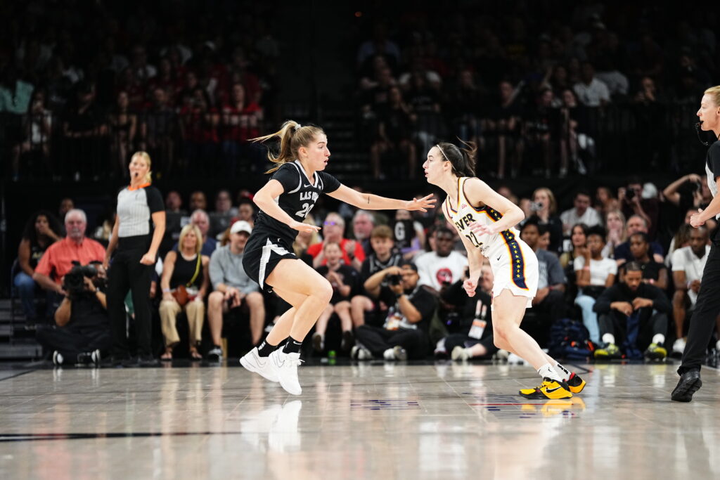 Kate Martin #20 of the Las Vegas Aces and Caitlin Clark #22 of the Indiana Fever look on during the game