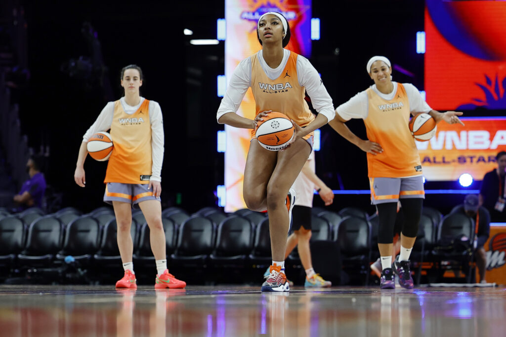 Team WNBA's Angel Reese lines up a shot while fellow rookie Caitlin Clark looks on.