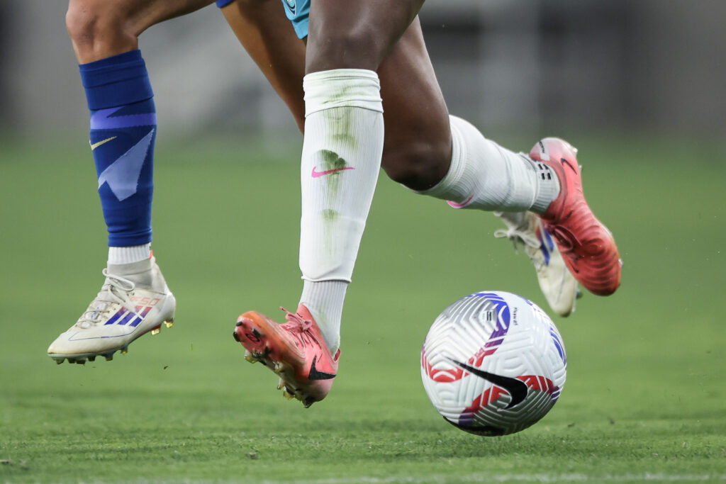 A close-up of two players' legs as one dribbles the ball across the NWSL field during a match.