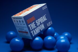 A box of Sequel tampons is posed amid a handful of blue racquet balls.