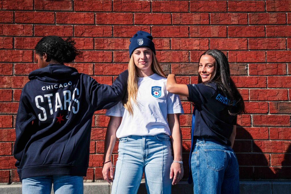 Three Chicago Red Stars players model clothing showcasing the team's new name and logo.