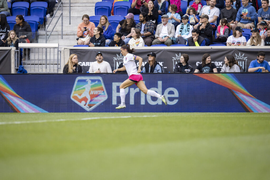 Former NWSL star Alex Morgan runs in front of an NWSL LGBTQ+ Pride logo