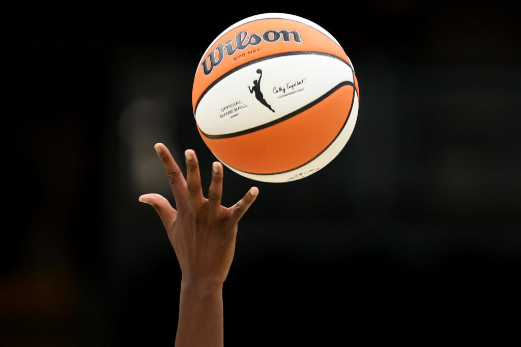 A hand reaches for a WNBA logo basketball midair