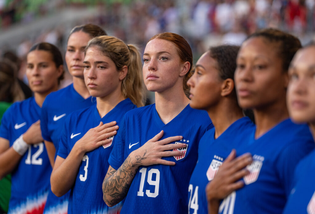 USWNT players Emily Sams, Emma Sears, Korbin Albert, Hal Hershfelt, Yazmeen Ryan, and Casey Krueger look line up for the national anthem.