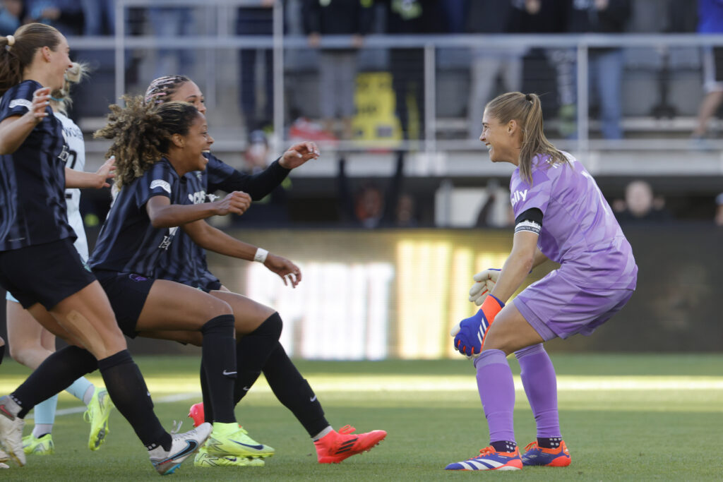 Goalkeeper Aubrey Kingsbury's Washington teammates swarm her in celebration after her penalty saves clinched the Spirit's 2024 NWSL semifinal win.