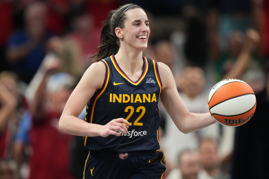 Indiana Fever star Caitlin Clark smiles while dribbling during a game.