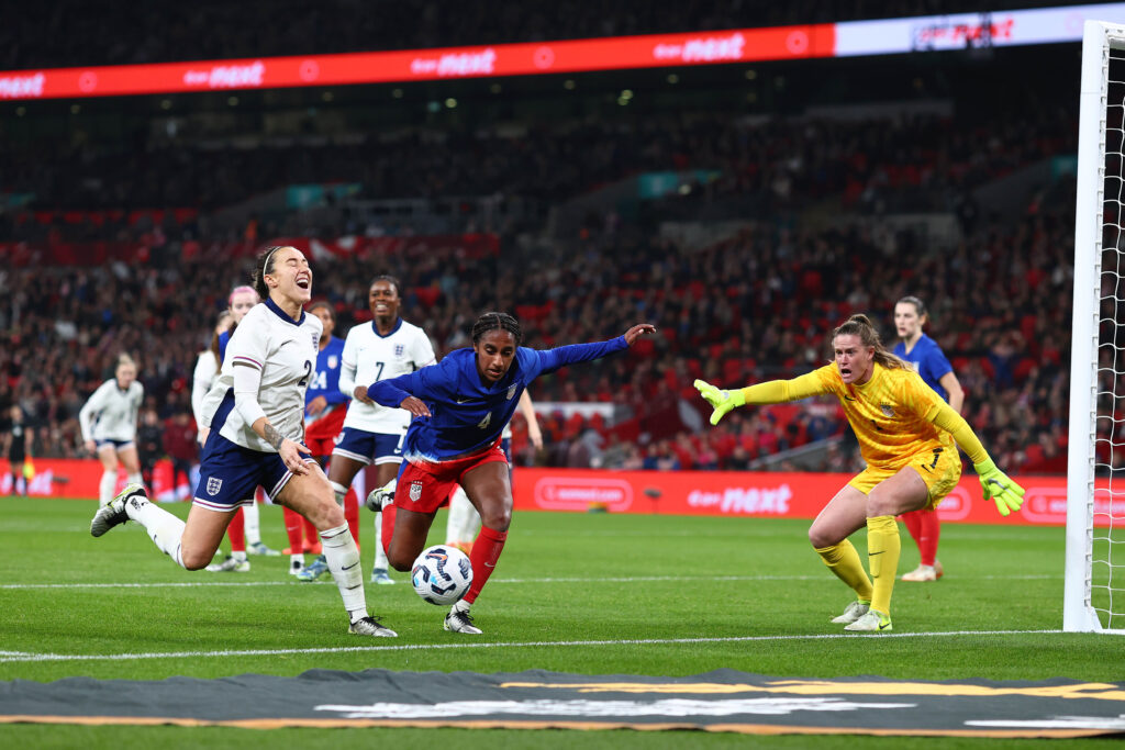 The USWNT's Naomi Girma and Alyssa Naeher and England's Lucy Bronze watch the ball roll out of play.