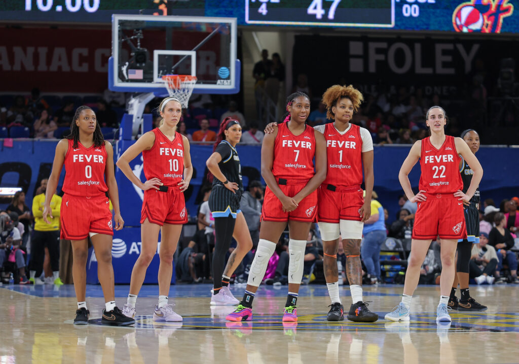 Indiana Fever players Caitlin Clark, NaLyssa Smith, Aliyah Boston, Kelsey Mitchell, and Lexie Hull watch a free throw during a game.