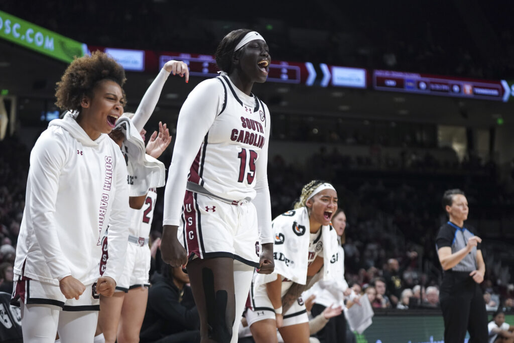 Tessa Johnson, Adhel Tac, and Te-Hina Paopao cheer on their South Carolina teammates during an SEC NCAA college basketball game.