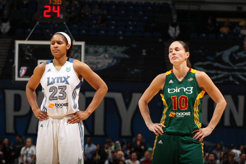 2025 Naismith Hall of Fame nominees Maya Moore and Sue Bird stand on the court during a 2012 WNBA Playoff game.