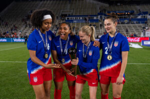 USWNT players Lily Yohannes, Cat Macario, Jenna Nighswonger, and Emily Fox hold the 2024 SheBelieves Cup trophy.