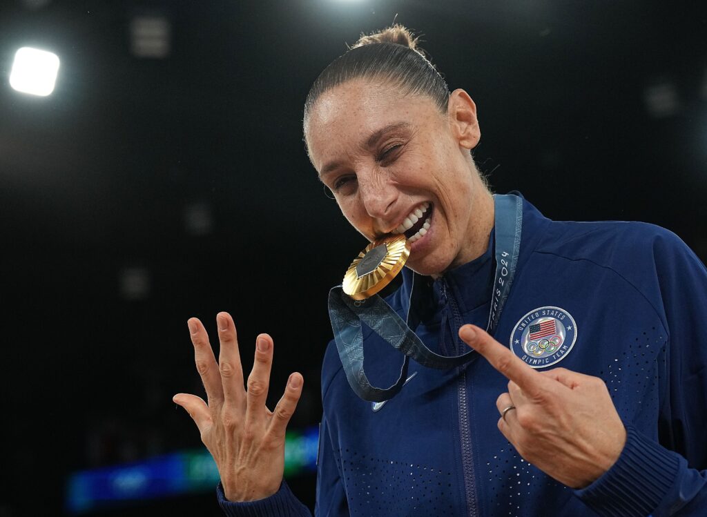 Team USA's Diana Taurasi bites her record-setting sixth straight Olympic gold medal at the 2024 Paris Games.