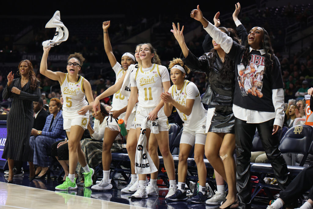 The Notre Dame basketball bench celebrates a basket during a game.