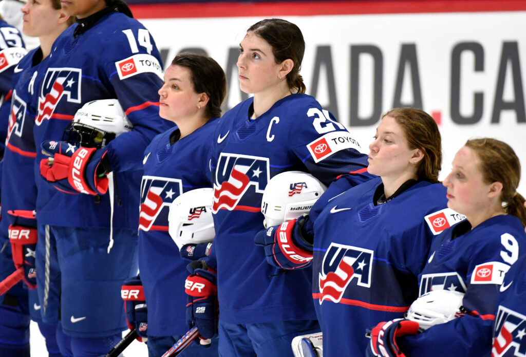 Team USA hockey players watch the flag be raised after a 2024 IIHF World Championship victory.